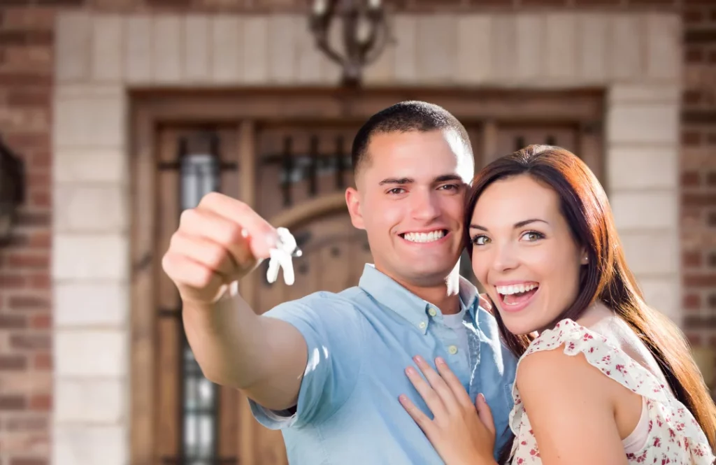 Two really happy people, a man and woman, holding house keys in front of a new house.