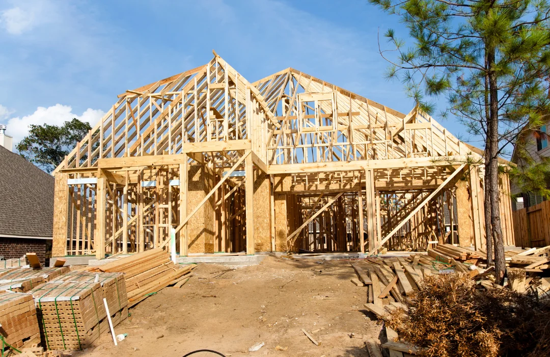 A house frame newly constructed on a dirt lot with a pine tree out front.