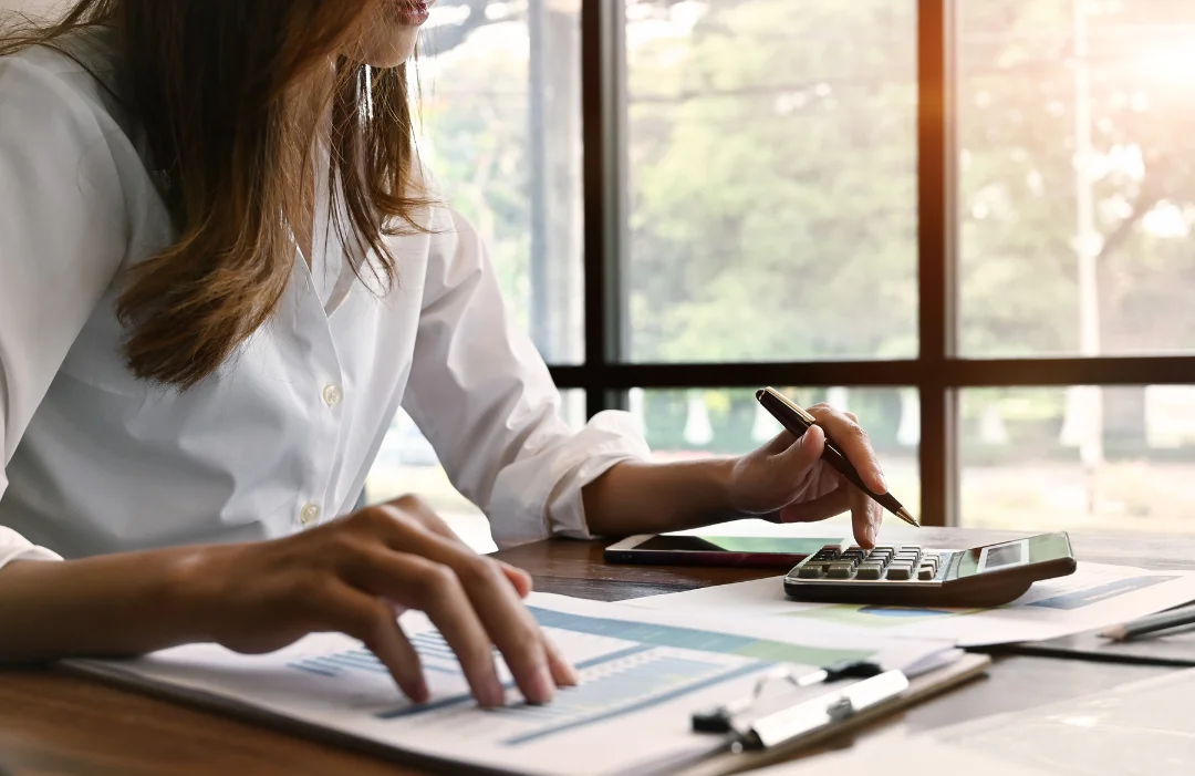 Young woman calculating costs with a calculator and a clipboard with a document of figures.