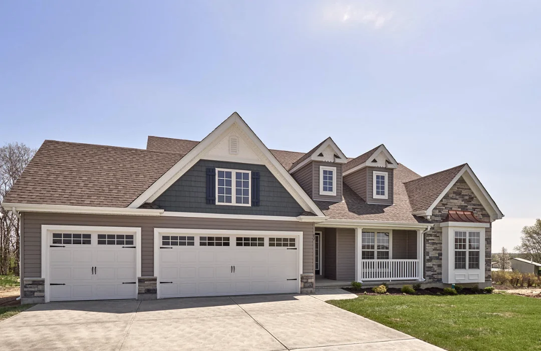 Large ranch home in 2-tone tan/blue, with 3-car garage, copper awnings, 2 carriage house gables, a front porch with railing