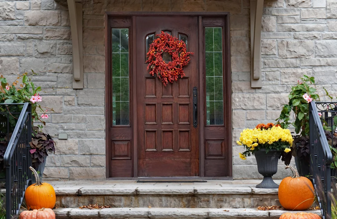 Front door of a home set in a stone front porch with pumpkins and mums on the steps.