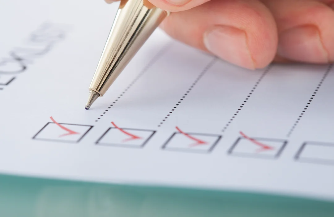 Gold ink pen being held by a man on a piece of paper that has check boxes with checkmarks in them.